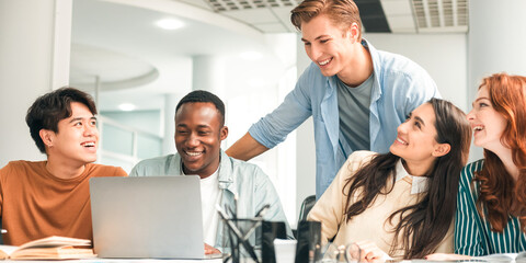 Positive Social Interaction. Cheerful international friends enjoying cooperation and collaboration, using pc laptop and talking, sharing ideas preparing group project in college library together