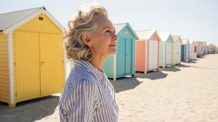 Elderly caucasian woman enjoys sunshine by colorful beach huts on sandy shore