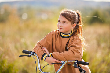 teenage girl leaning on bicycle handlebars against natural landscape