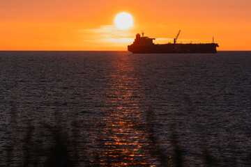 The silhouette of a huge ship slowly crosses the horizon and the sun path on the water during a...
