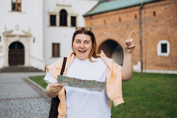 Happy young woman with map in old town. Holidays and tourism concept. Female tourist searching direction on location map while traveling abroad in summer