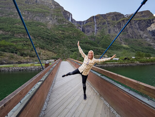 A female traveler stands on a modern architectural bridge crossing a mountain river, admiring the...
