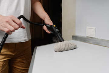 Cropped shot of housewife in casual clothes using steam cleaner, sanitizing kitchen countertop with...