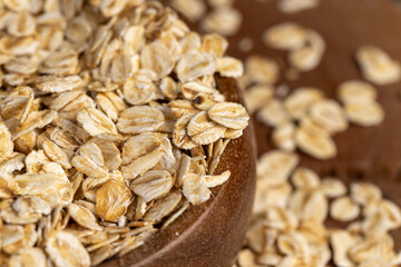wooden bowl with oatmeal flakes for making porridge, scattered dry cereal flakes from oats,...