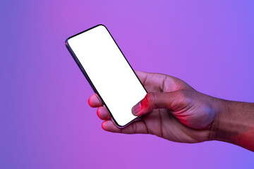 Naklejka na ściany i meble Black Male Hand Holding Smartphone With Glowing White Screen Under Neon Light Over Purple Background, Unrecognizable African American Man Showing Free Copy Space For Your App Design, Mockup Image