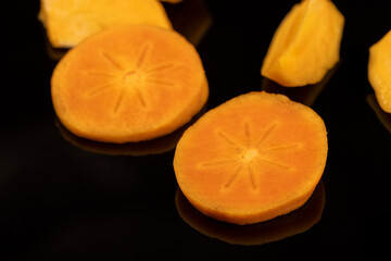 peeled ripe juicy persimmons persimmons are reflected on the black mirror surface, close up