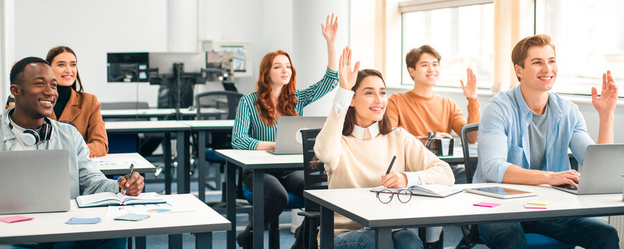 Smiling multicultural people raising hands to agree or to ask questions at modern seminar in office, diverse mixed race group of men and women sitting at desk with laptop computer listening to speaker - Powered by Adobe