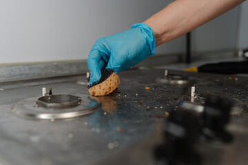 Close-up cropped shot of unrecognizable man in gloves scrubbing dirty gas stove with sponge,...