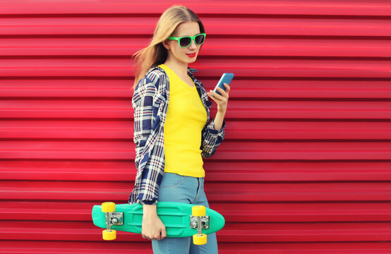 Modern young woman using smartphone, stylish teenage girl holding mobile phone with skateboard