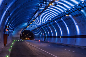 Illuminated modern roadway tunnel interior. View of a modern tunnel with blue lighting accentuating its curved walls and ceiling. The image suitable for transportation urban and infrastructure.