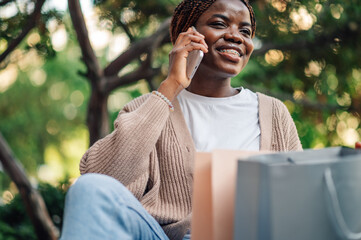 Smiling young woman talking on mobile phone holding shopping bags in a park