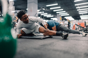 Two male athletes stretching legs in modern gym