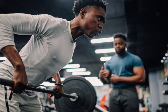 Determined male athlete lifting weights with personal trainer in gym