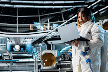 Female astronaut scientist running telemetry software on notebook. Woman researcher wearing...