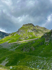 Arched structures, part of mountain road, blend seamlessly into lush green alpine slope. Rugged...