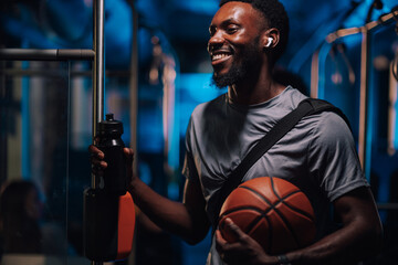 Smiling basketball player holding ball and water bottle on bus at night