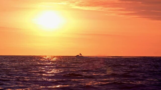 Silhouette of people riding jet skis at sunset far from the shore.