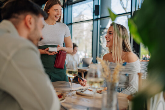 Waitress holding pos terminal accepting payment from customers in restaurant
