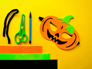 DIY Halloween mask. Handmade orange pumpkin mask made of felt on a yellow background for Halloween....