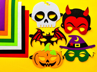 Halloween. DIY Felt Halloween Masks. Felt masks and felt sheets are lying on yellow background. Set of Various Masks, monsters, Pumpkin, Devil, Witch, Skeleton, Bat, DIY Toys, Game Accessories.