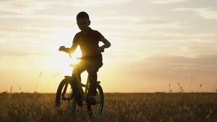 Little boy rides bicycle on grass field. Active kid, cyclist plays, rides at sunset. Childs feet are pedaling. Pedaling, bicycle wheel. Children travel. Physical exercise. Family in park. Free play