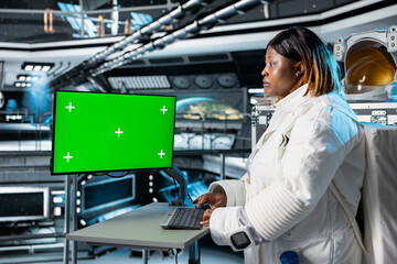 Astronaut reviewing spacecraft analytics on green screen monitor to ensure safe operation during long distance space travel. Woman in orbit station uses mockup display during cosmic journey