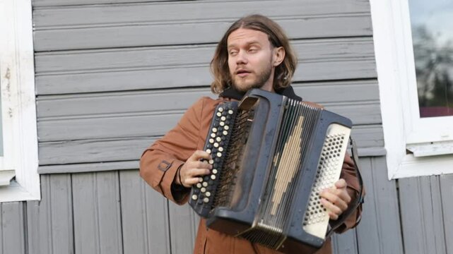 A long-haired man plays the accordion outdoors
