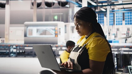 Woman engineer in photovoltaics factory uses tracking software on laptop to diagnose malfunctioning...