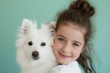 Beautiful smiling girl hugging fluffy white spitz dog against solid pastel green background, both looking at camera with joyful expressions