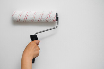 Female arm holding a paint roller against a plain white wall, DIY renovation concept