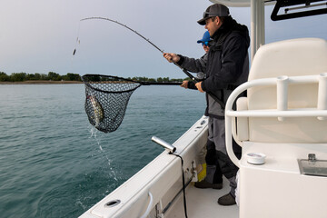 Two men netting a fish while fishing on a boat.
