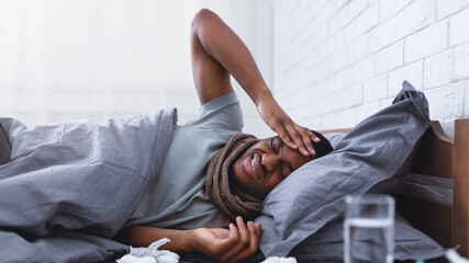 Ill African American Guy Having Severe Headache Suffering From Pain Touching Aching Head Lying In Bed At Home. Migraine During Influenza And Cold Concept. Selective Focus