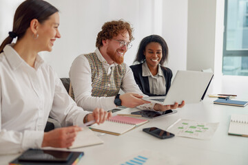 A diverse group is eagerly collaborating in a modern office, sharing ideas and engaging with tech tools
