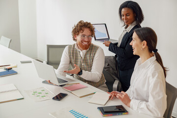 In a bright office, a diverse team collaborates enthusiastically, using laptops and handling...