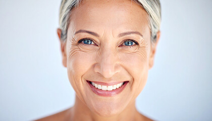 Radiant mature woman with sparkling blue eyes and captivating charm smiles warmly, exuding confidence and joy in bright, soft background