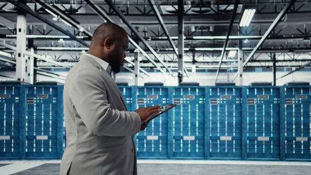 Cheerful server room engineer troubleshooting backend operations using software on tablet. Jolly data center programmer compiling software patches to fix bugs using device, camera A