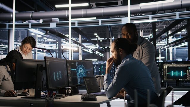 Data center engineers use laptop, collaborating on doing AI software updates. Server room teamworking colleagues doing brainstorming, optimizing infrastructure using artificial intelligence, camera A