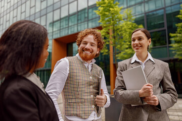 Three diverse professionals are actively engaging in a lively discussion outdoors near a modern...