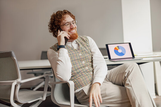 A professional man in a stylish vest is discussing business matters on his phone in a modern office