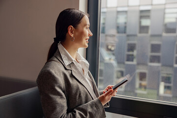 A professional woman in a stylish suit is focused on her phone, reflecting on work in a modern...