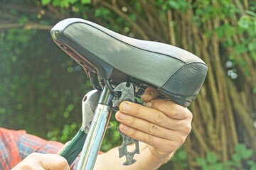 man hand holding black grey bicycle leather saddle with open-end wrench over bicycle on summer street