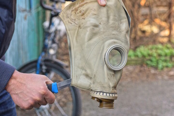 hands of one man holding one old gray army rubber gas mask with an knife in his head on an autumn street