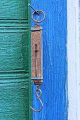 one old long brown iron canter scale in rust hanging on green blue wooden wall outside