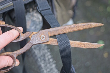 hand holding old brown big rusty iron scissors cutting black strap on bag on summer street