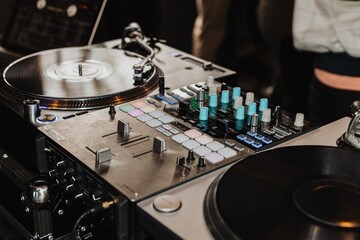 Close-up of DJ turntable and mixer setup with vinyl records, faders and colorful control knobs at a...