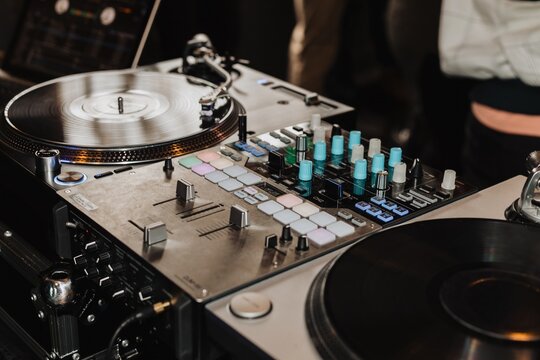 Close-up of DJ turntable and mixer setup with vinyl records, faders and colorful control knobs at a live event
