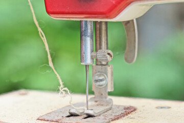 old red toy metal sewing machine with white thread and needle on green background
