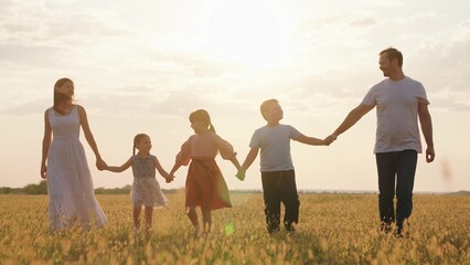 Happy family with children walks in grass field in summer. Big family, group of people in nature. Dad mom daughter son go hand in hand outdoors in autumn. Parental care for children. Active family