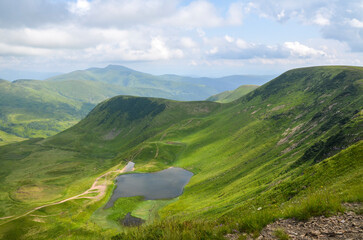 Peaceful mountain valley featuring vivid green meadows, winding paths, and tranquil Dogyaska lake...