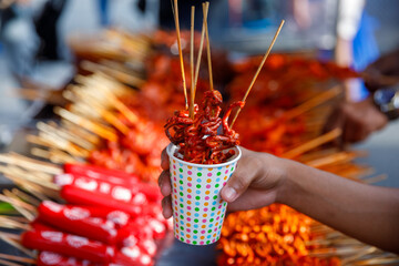 Filipino street food in takeaway paper cup with grilled chicken intestines on skewers, ideal for food delivery, travel blogs, or menu design